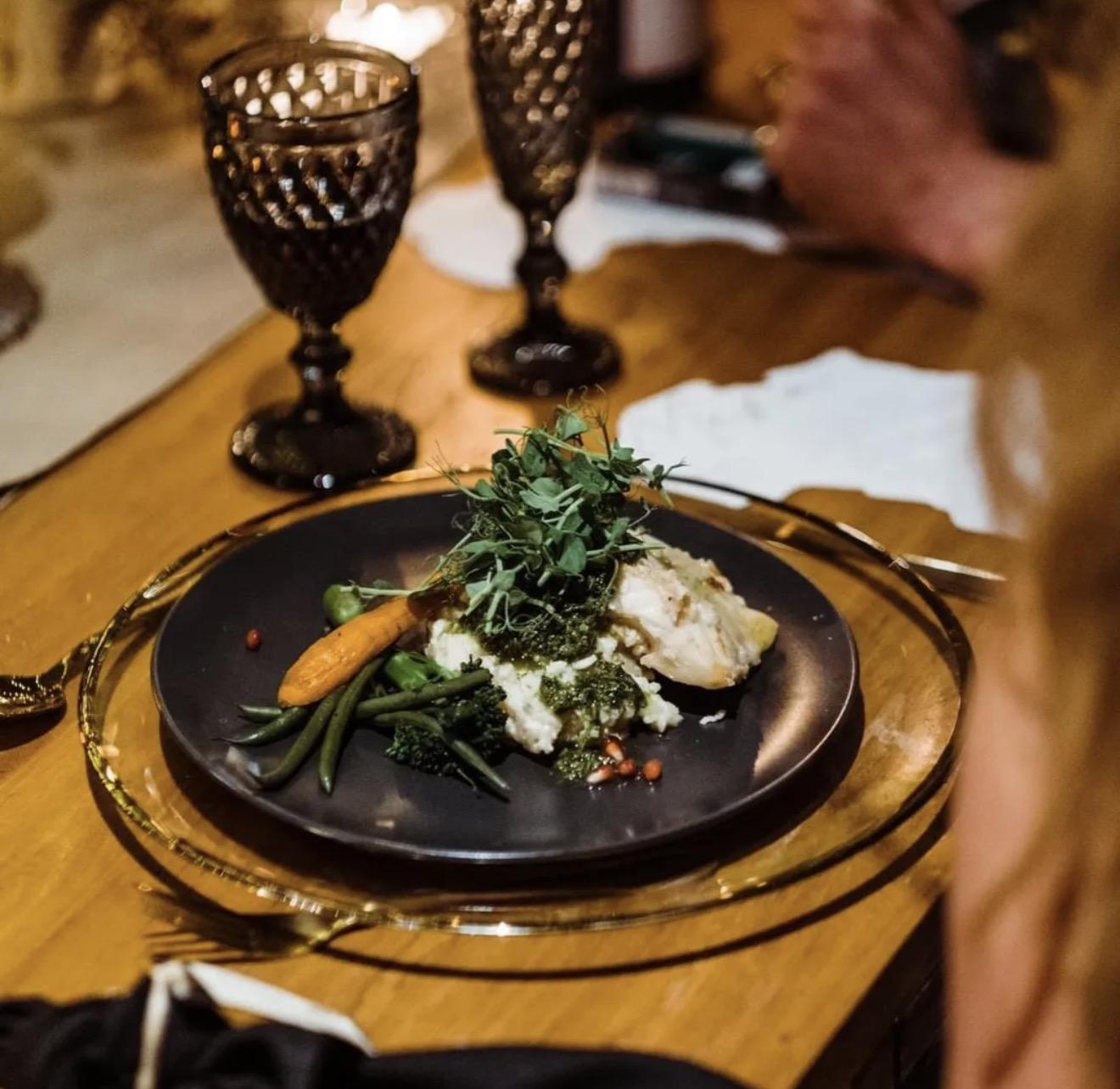A plated meal with vegetables, greens and a herb sauce at a dressed table