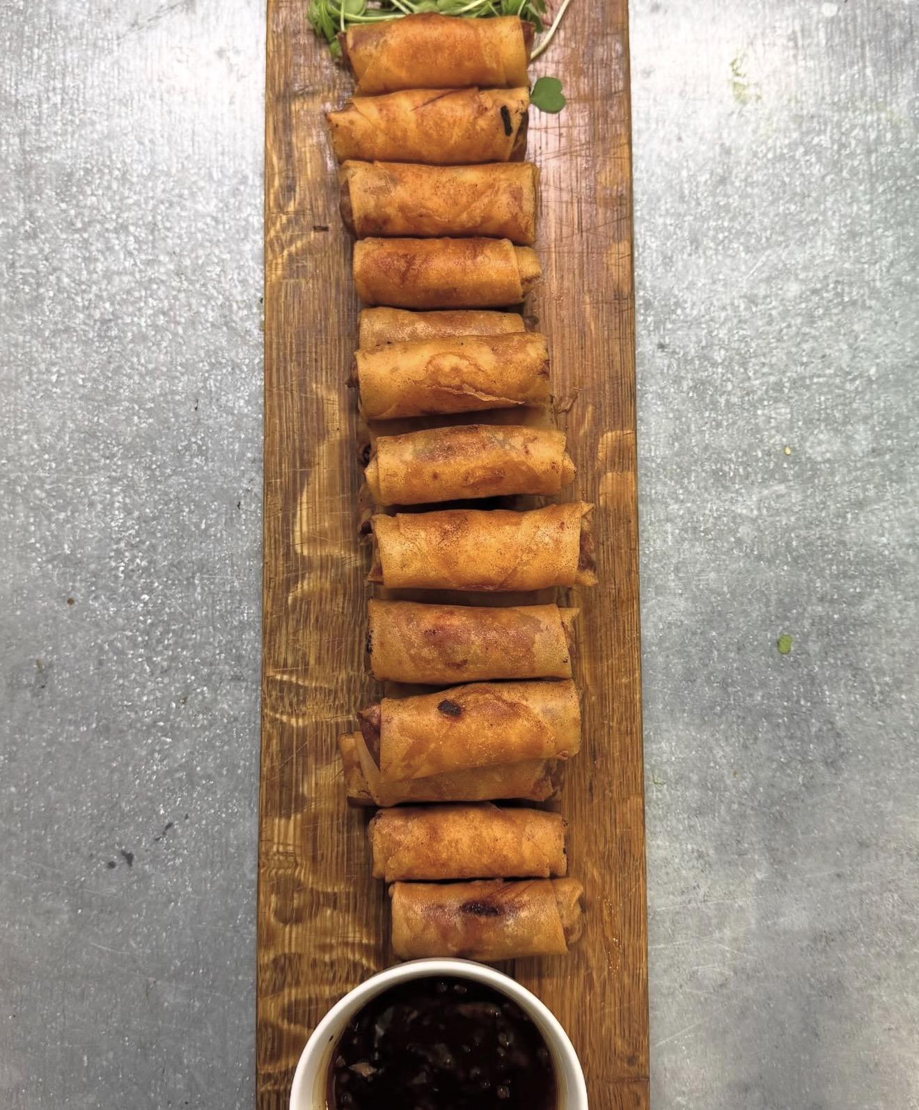 A long wooden platter of golden canapé rolls with dipping sauce