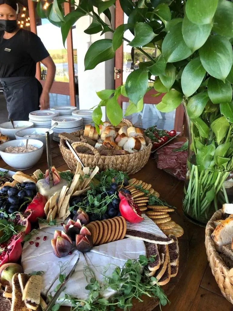 A harvest table with cheeses, crackers, bread baskets, grapes, figs and greenery, with a server beside stacked plates
