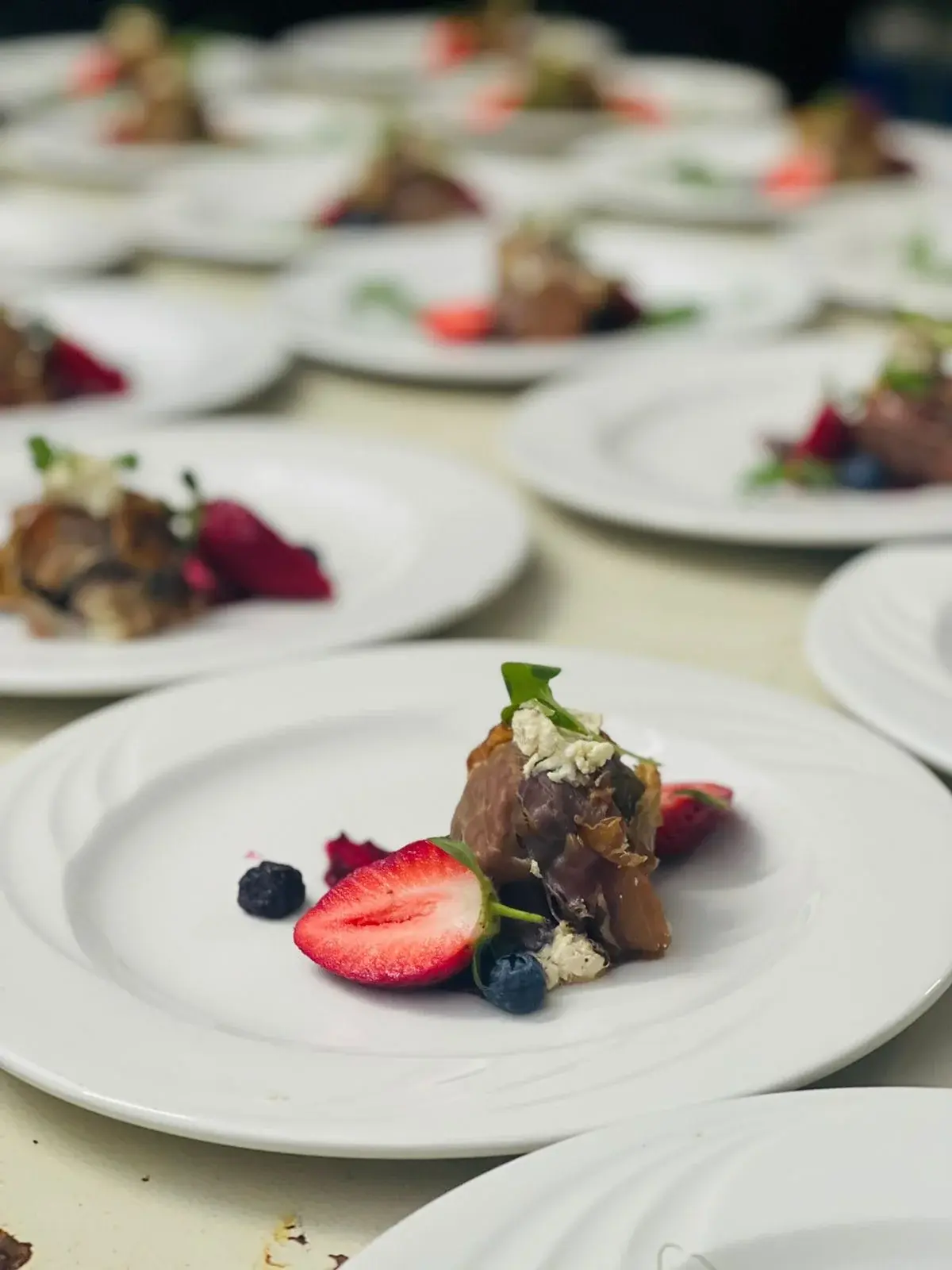 Rows of white plates with individually presented starters, strawberries, blueberries and greens