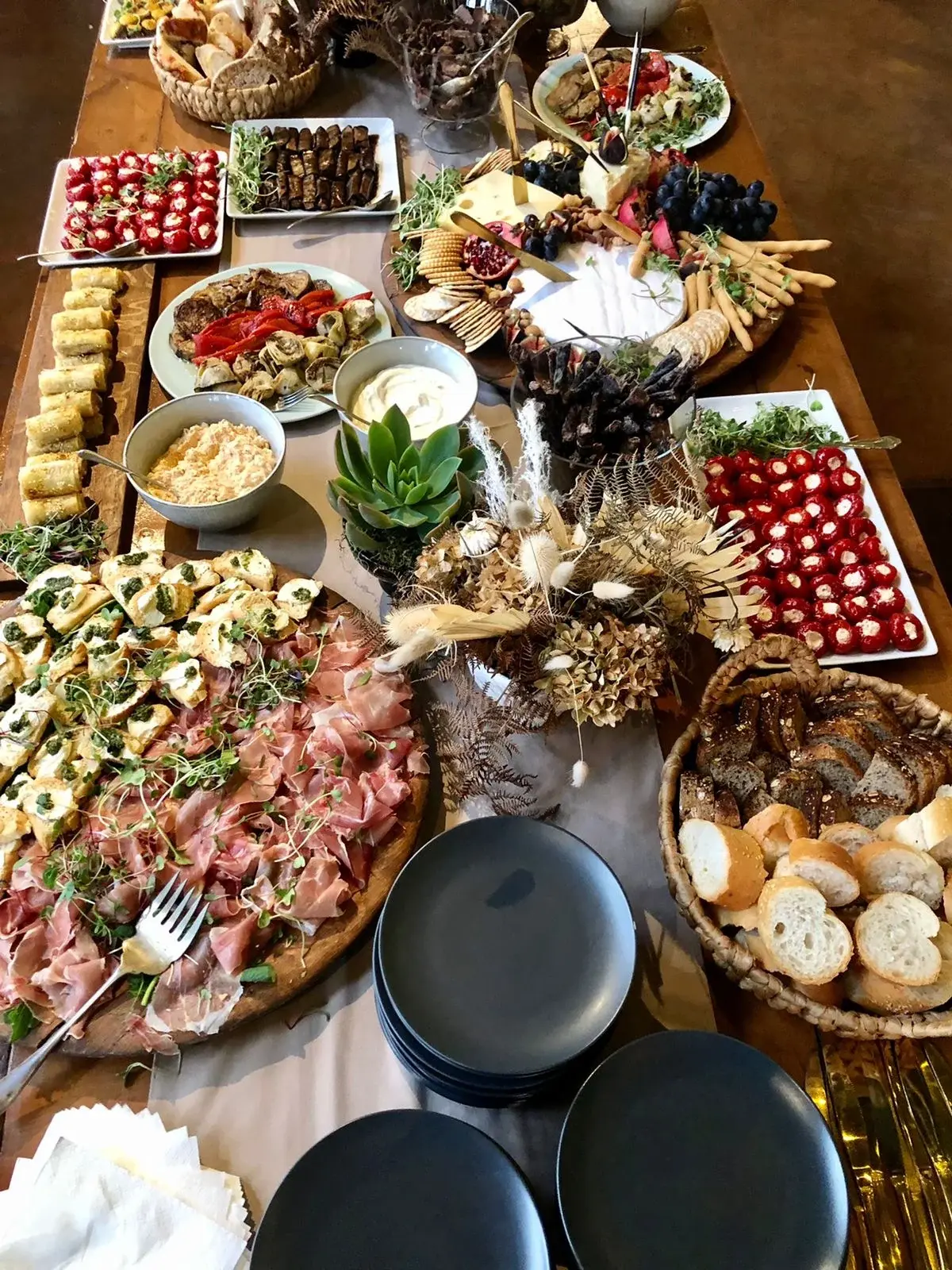 An overhead view of a harvest table with cheeses, crackers, sliced meats, bread baskets and vegetable platters