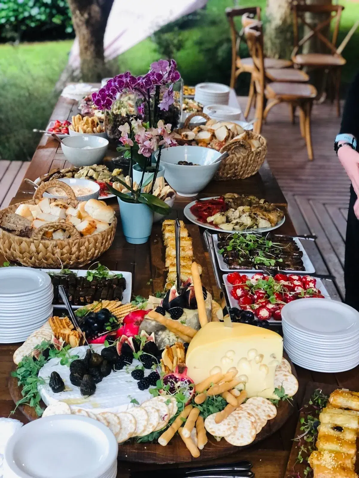 A wooden harvest table with cheeses, bread baskets, crackers, vegetable platters and purple orchids