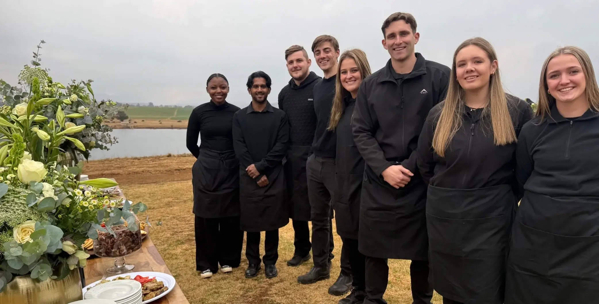 The Fat Aubergine catering team beside an outdoor food table and flowers
